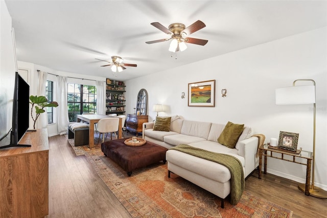 living area with baseboards, wood-type flooring, and ceiling fan