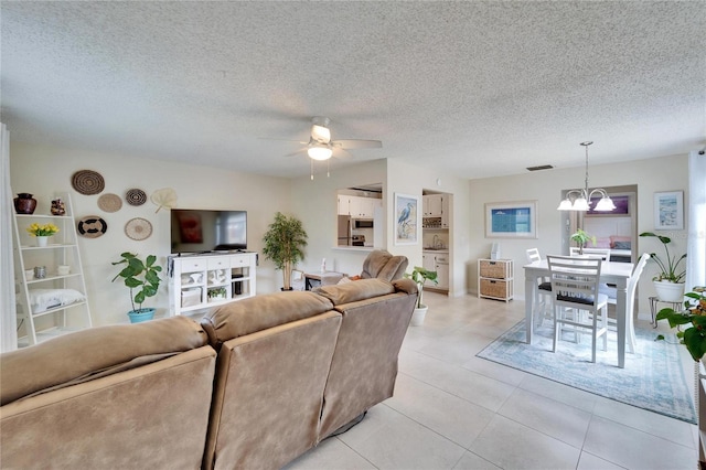 living area with light tile patterned floors, ceiling fan with notable chandelier, visible vents, and a textured ceiling