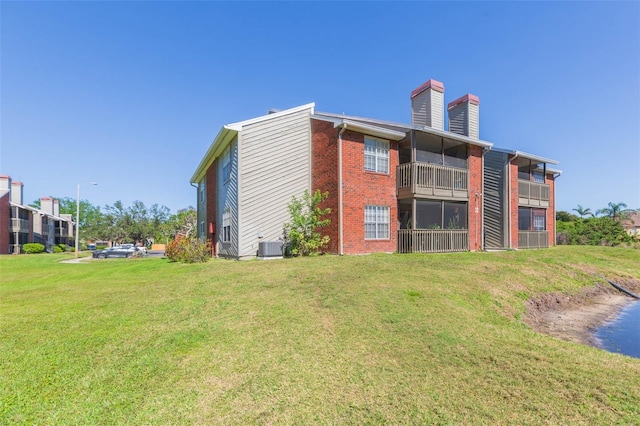 rear view of house with brick siding, central AC unit, a lawn, and a chimney