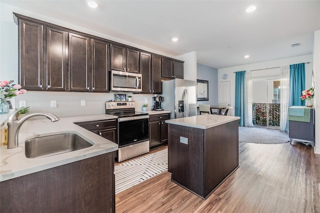 kitchen featuring a kitchen island, dark brown cabinetry, light wood-type flooring, stainless steel appliances, and a sink