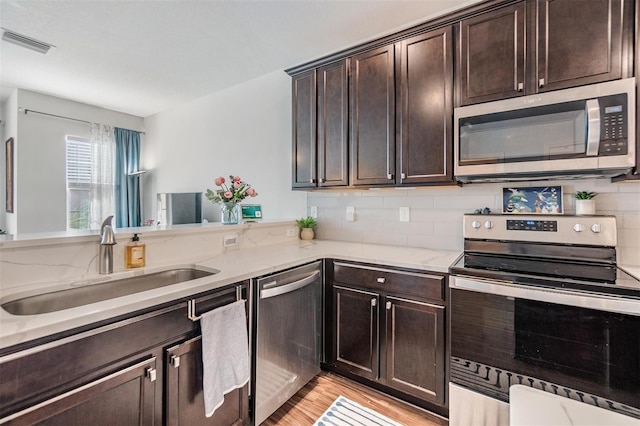 kitchen featuring visible vents, a sink, stainless steel appliances, dark brown cabinetry, and light stone countertops