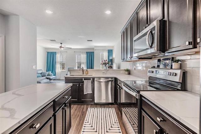 kitchen featuring dark wood-type flooring, light stone countertops, appliances with stainless steel finishes, a peninsula, and a sink