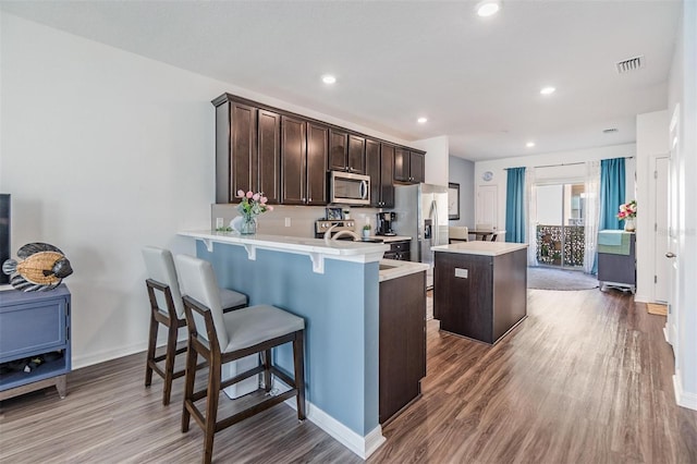 kitchen featuring visible vents, a kitchen island, stainless steel appliances, dark brown cabinetry, and light countertops