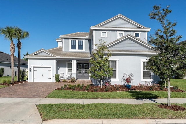 view of front of property with french doors, decorative driveway, an attached garage, and stucco siding