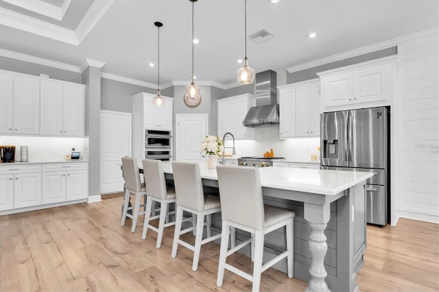 kitchen with visible vents, stainless steel appliances, white cabinetry, wall chimney range hood, and light wood-type flooring