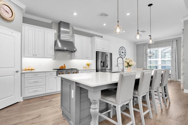 kitchen featuring visible vents, crown molding, wall chimney range hood, a center island with sink, and stainless steel appliances