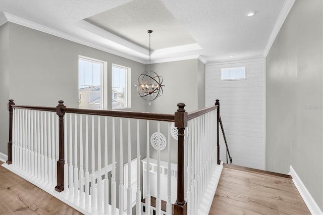 stairs with wood finished floors, baseboards, an inviting chandelier, a tray ceiling, and ornamental molding