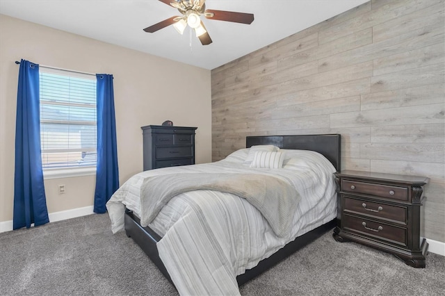 carpeted bedroom with wooden walls, a ceiling fan, and baseboards