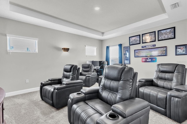 cinema room with a tray ceiling, baseboards, visible vents, and light carpet