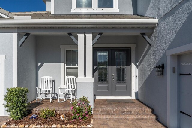 entrance to property featuring covered porch, stucco siding, and french doors