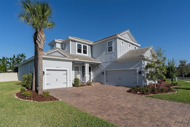 traditional home featuring a front lawn, fence, stucco siding, decorative driveway, and an attached garage