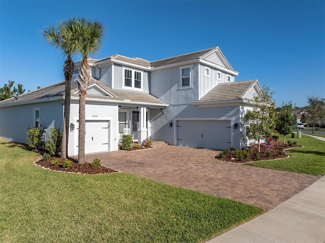 traditional-style home featuring stucco siding, decorative driveway, an attached garage, and a front lawn