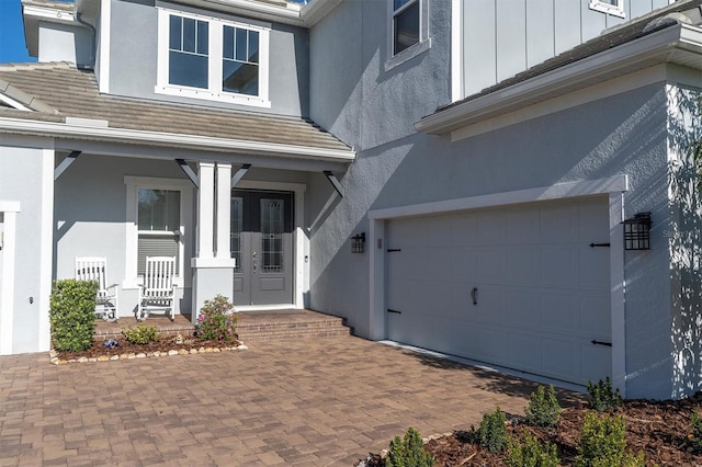 property entrance with stucco siding, french doors, covered porch, board and batten siding, and a garage