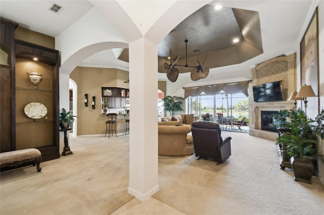 living area with baseboards, visible vents, arched walkways, light carpet, and a tiled fireplace