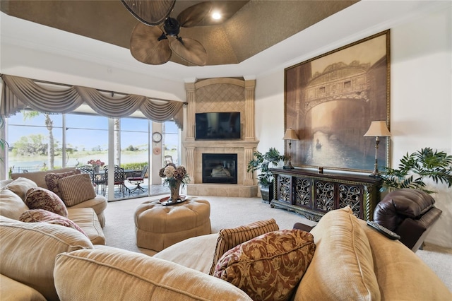 carpeted living area with a tiled fireplace, a raised ceiling, and a ceiling fan