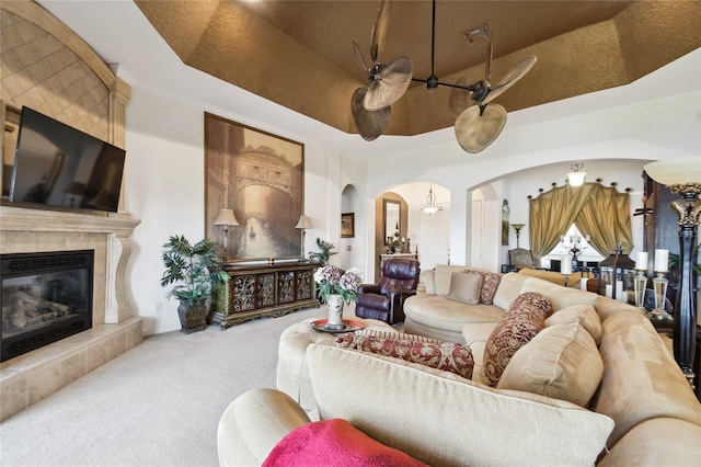 living room with a tray ceiling, carpet flooring, arched walkways, and a tile fireplace