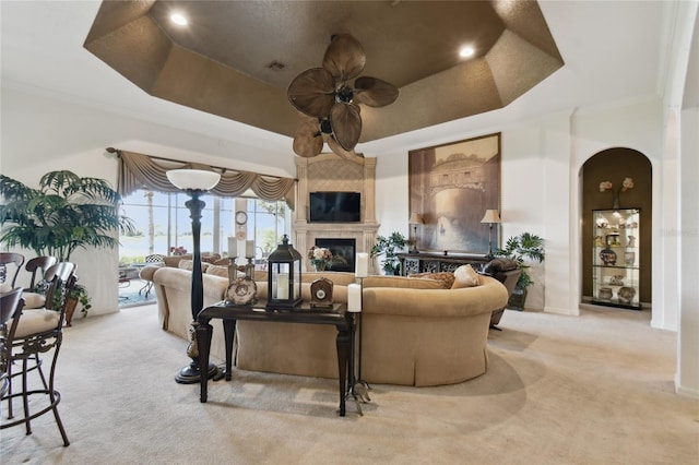 carpeted living room with arched walkways, recessed lighting, a ceiling fan, and a tray ceiling