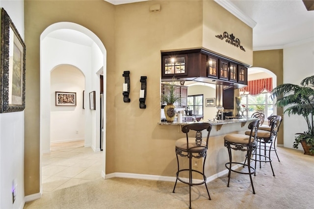 kitchen featuring arched walkways, dark brown cabinets, glass insert cabinets, light carpet, and a kitchen breakfast bar