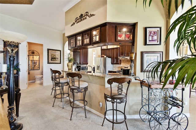 kitchen with light colored carpet, ornamental molding, a kitchen breakfast bar, a peninsula, and stainless steel refrigerator with ice dispenser