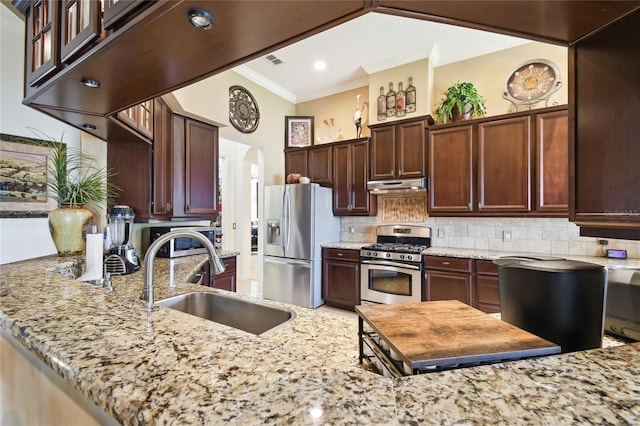 kitchen with under cabinet range hood, ornamental molding, arched walkways, stainless steel appliances, and a sink