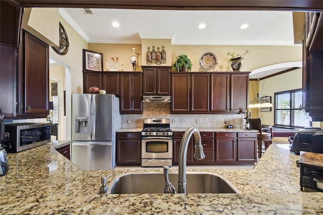 kitchen with under cabinet range hood, decorative backsplash, appliances with stainless steel finishes, and a sink