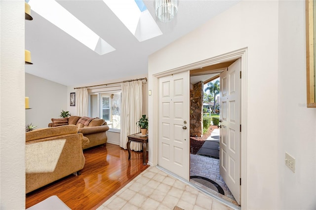 entryway with baseboards, vaulted ceiling with skylight, and light wood-style flooring