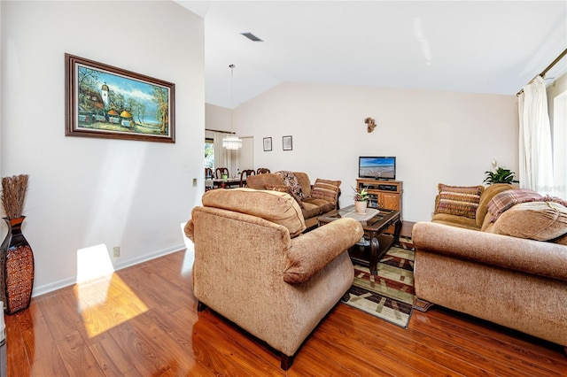 living area with vaulted ceiling, baseboards, visible vents, and wood finished floors