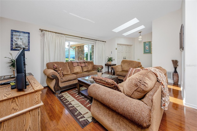 living room with lofted ceiling with skylight, wood finished floors, and visible vents