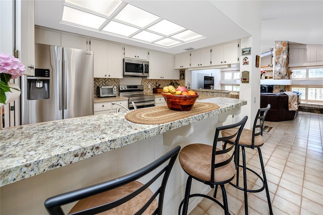 kitchen with backsplash, a breakfast bar area, light tile patterned floors, appliances with stainless steel finishes, and white cabinets