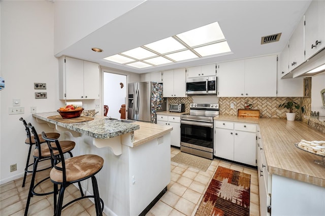 kitchen featuring visible vents, tasteful backsplash, stainless steel appliances, a peninsula, and light countertops