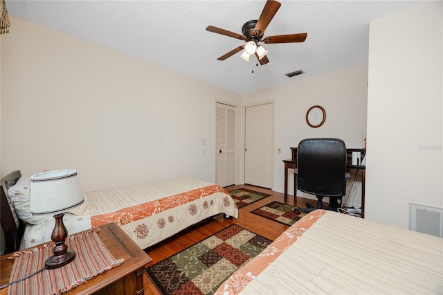 bedroom with ceiling fan, visible vents, a textured ceiling, and wood finished floors