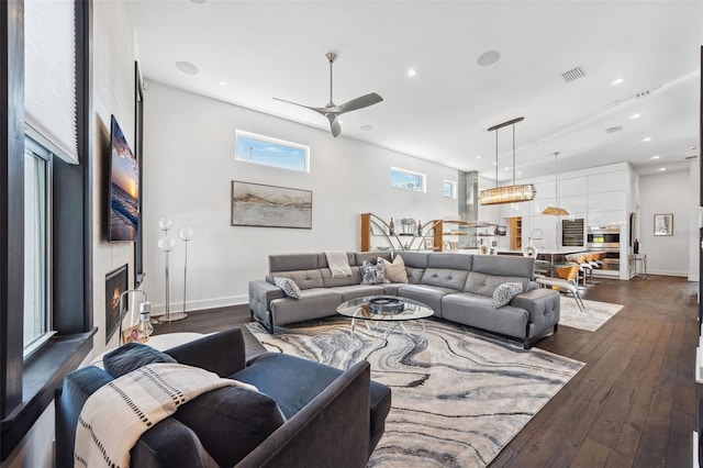 living area featuring dark wood-type flooring, a ceiling fan, baseboards, and a large fireplace