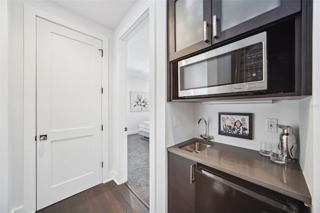 bar with dark wood-type flooring, baseboards, appliances with stainless steel finishes, wet bar, and a sink