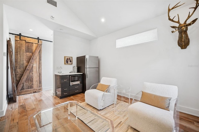 living area with visible vents, light wood-type flooring, lofted ceiling, and a barn door