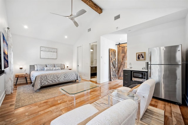 bedroom with beamed ceiling, visible vents, light wood-style flooring, freestanding refrigerator, and a barn door