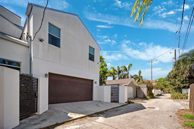 view of property exterior with stucco siding, driveway, an attached garage, and fence