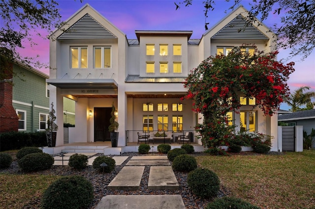 back of property at dusk featuring a lawn, covered porch, and stucco siding