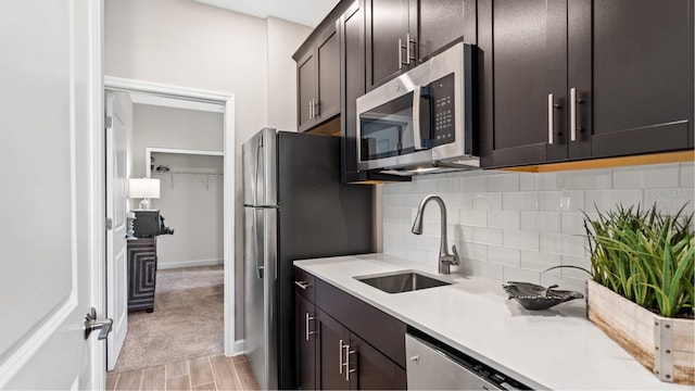 kitchen featuring a sink, appliances with stainless steel finishes, light countertops, decorative backsplash, and light colored carpet