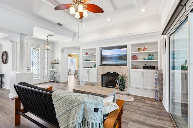 living area featuring wood finished floors, visible vents, a fireplace with raised hearth, ceiling fan, and crown molding