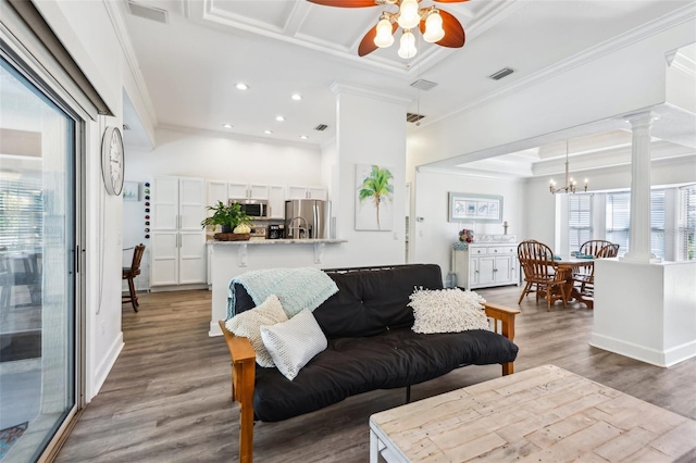 living room with ornamental molding, ceiling fan with notable chandelier, wood finished floors, recessed lighting, and decorative columns