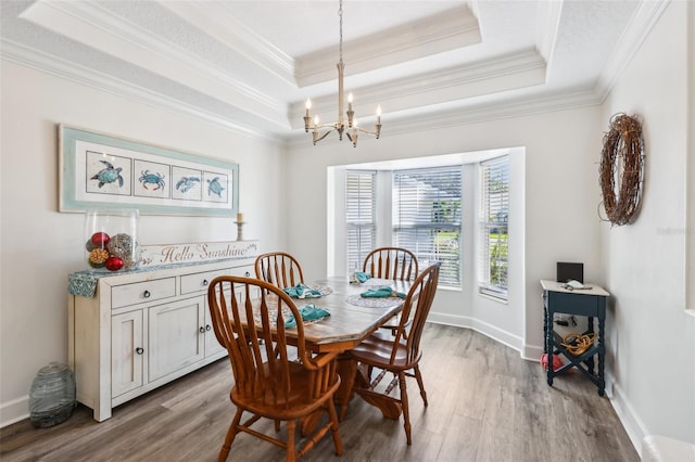 dining area featuring a tray ceiling, crown molding, a notable chandelier, and wood finished floors