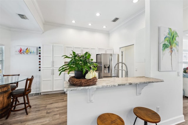 kitchen featuring a breakfast bar area, a peninsula, ornamental molding, stainless steel refrigerator with ice dispenser, and white cabinetry