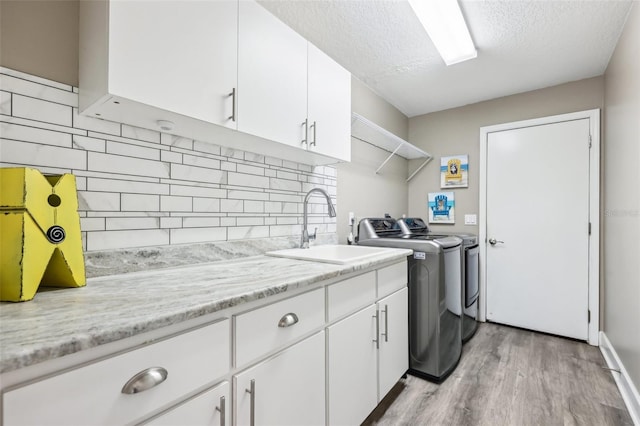 clothes washing area featuring light wood finished floors, cabinet space, a textured ceiling, independent washer and dryer, and a sink