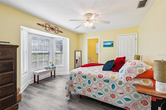 bedroom featuring a ceiling fan, wood finished floors, visible vents, baseboards, and a textured ceiling