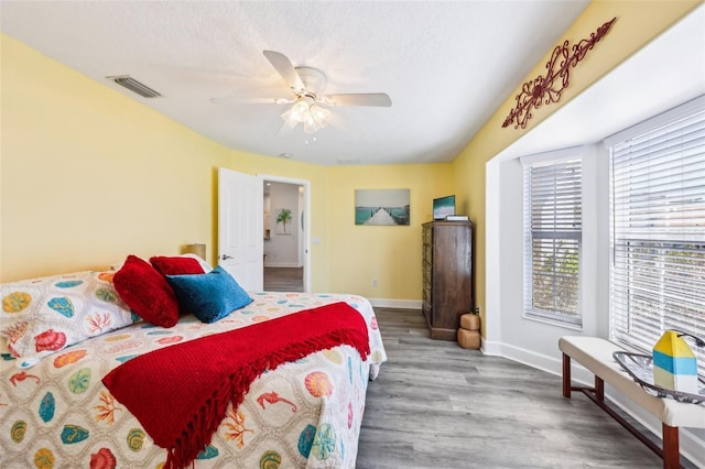 bedroom featuring a ceiling fan, wood finished floors, visible vents, baseboards, and a textured ceiling