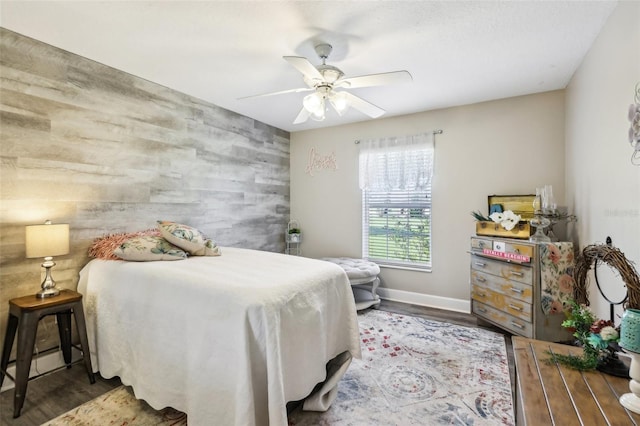 bedroom featuring a ceiling fan, wood finished floors, wood walls, baseboards, and an accent wall