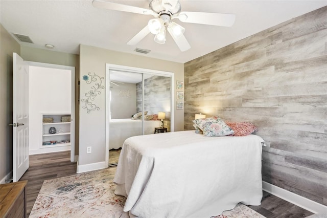 bedroom with a closet, visible vents, ceiling fan, and wooden walls