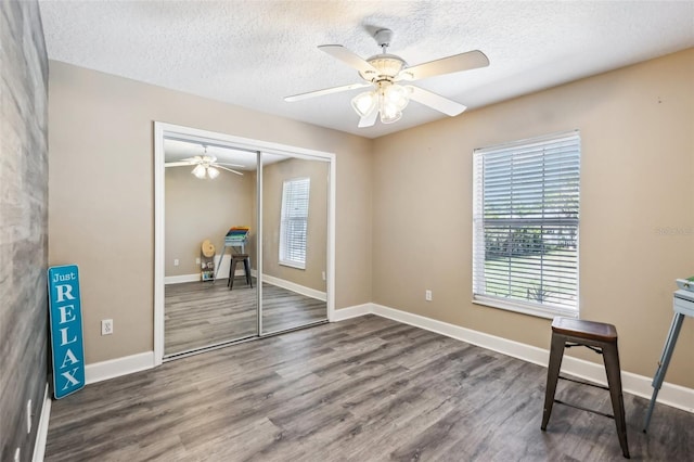 unfurnished bedroom featuring a textured ceiling, wood finished floors, a closet, baseboards, and ceiling fan