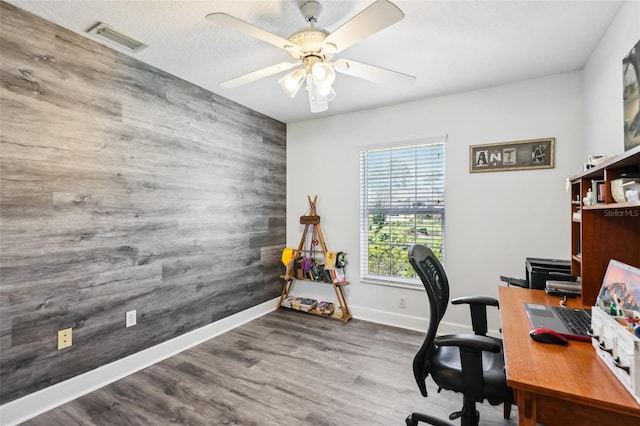 office space with visible vents, wood finished floors, baseboards, ceiling fan, and an accent wall