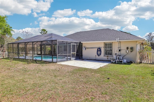 back of house featuring a shingled roof, stucco siding, glass enclosure, a yard, and a patio area